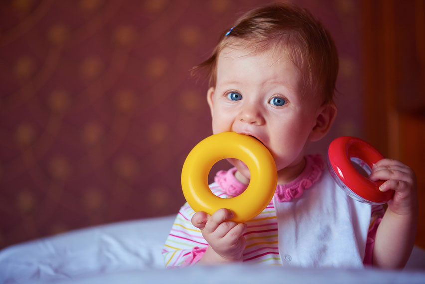 1 year old girl with first teeth biting a toy