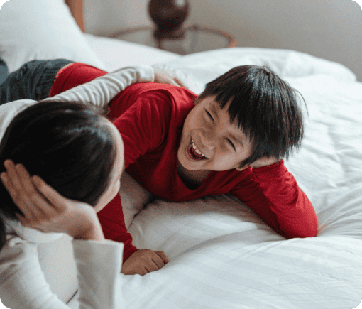 Two children lying on a bed, laughing and smiling.