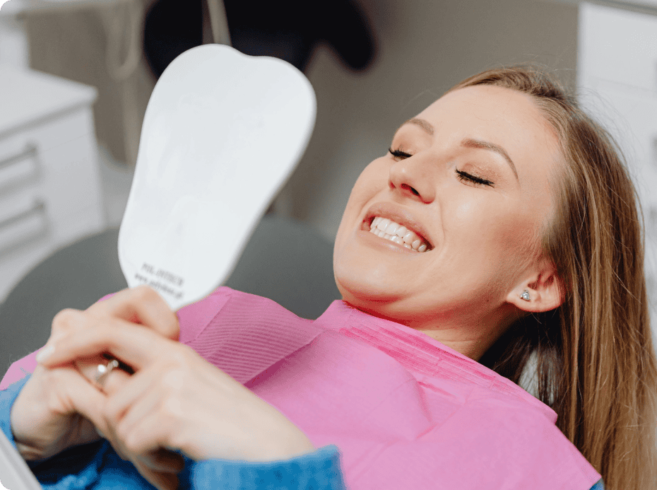 A woman admiring her teeth and smile after dental treatment in a mirror the doctor gave her.